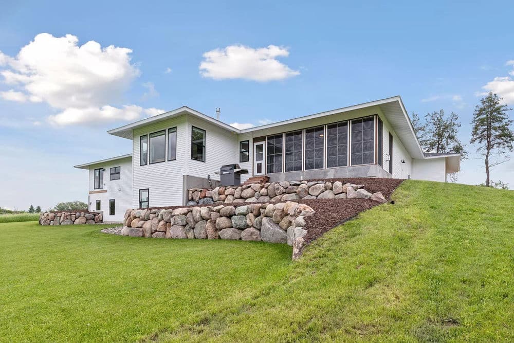 Modern white house with stone landscaping and scenic grassy yard under a blue sky.