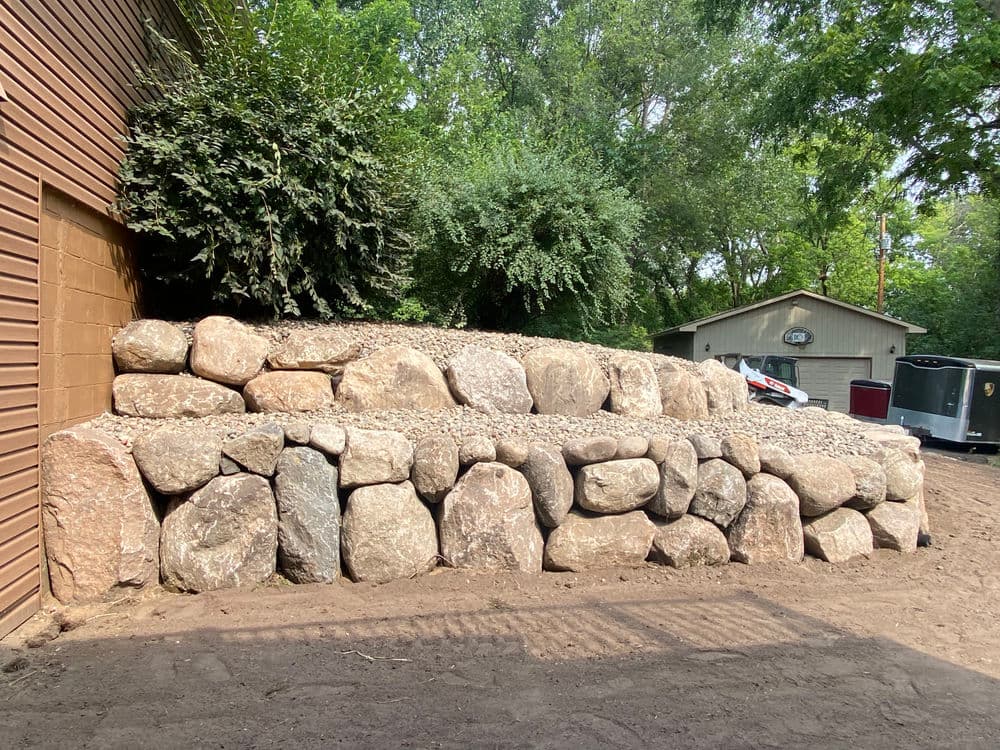 Landscaped rock retaining wall with gravel and lush greenery in background.