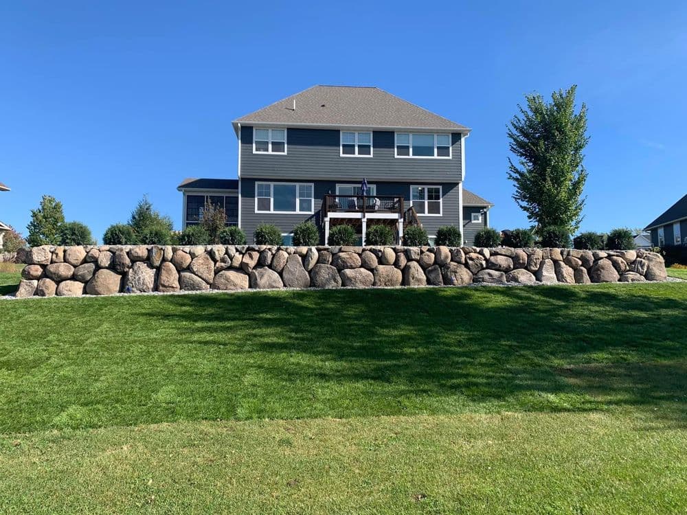 Modern two-story house with stone wall and well-maintained lawn under clear blue sky.