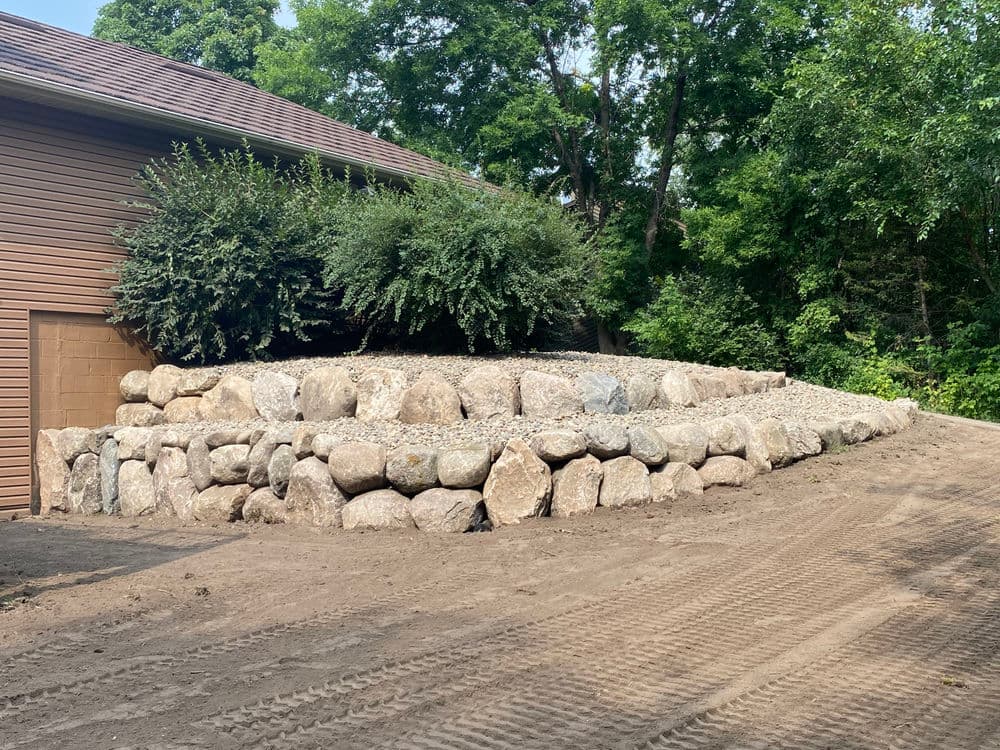 Stone retaining wall with plants beside a home, set in a landscaped outdoor area.