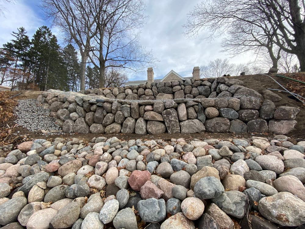 Rock retaining wall with layered stone design in a landscaped garden setting.