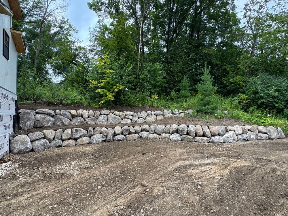 Stone retaining wall in a gravel landscape surrounded by greenery and trees.