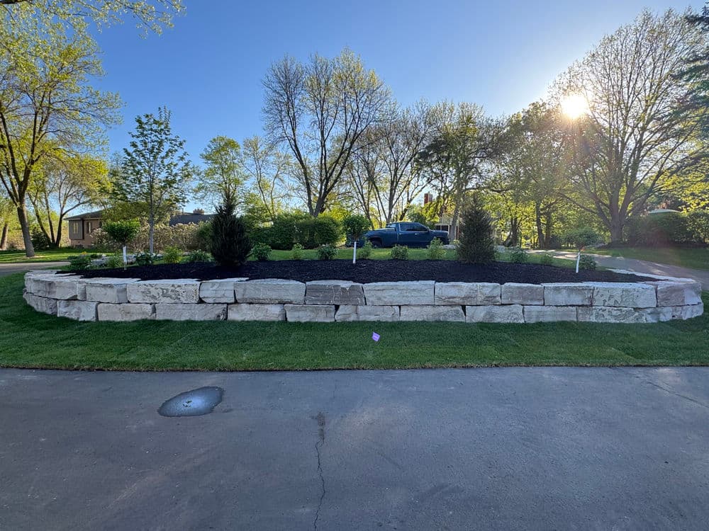 Circular stone garden bed surrounded by grass, trees, and a blue car in the background.