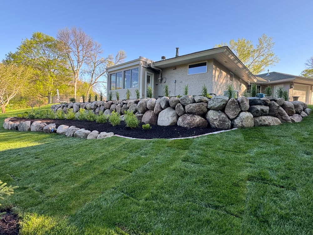 Modern landscaping with a stone wall, greenery, and a well-manicured lawn in front of a house.