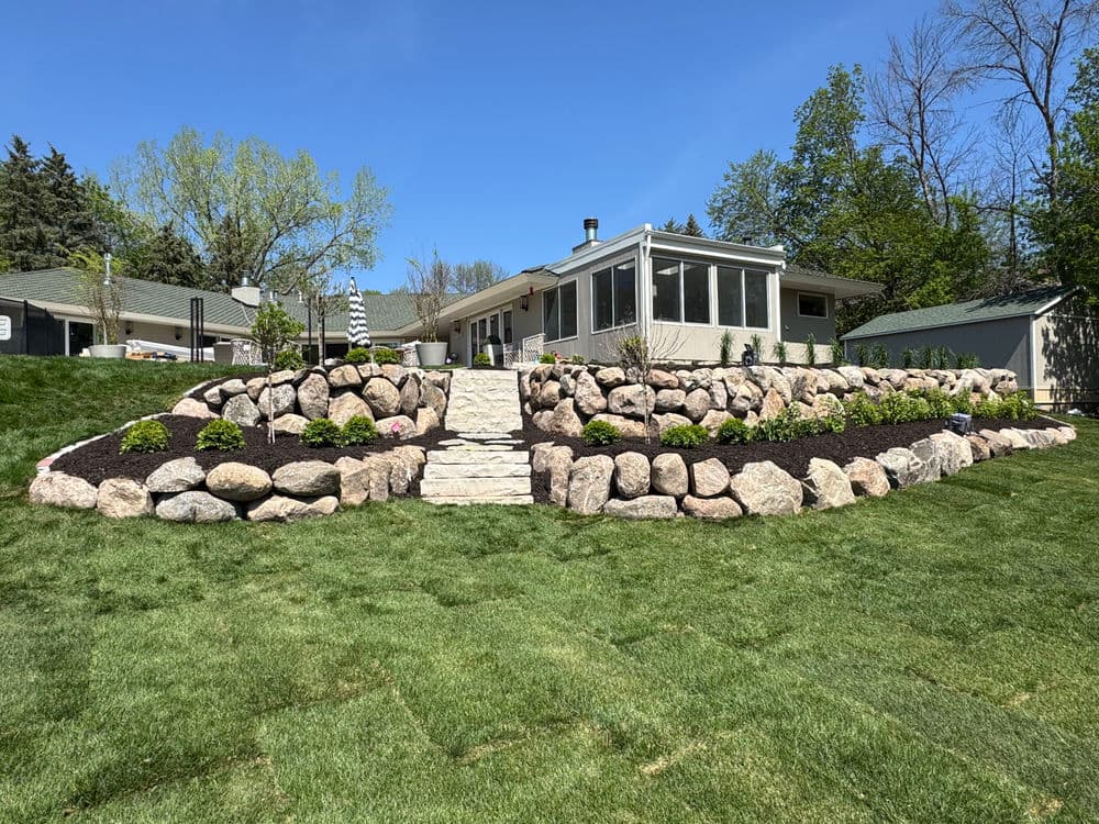 Landscape design featuring a stone retaining wall, lush grass, and a modern home in the background.