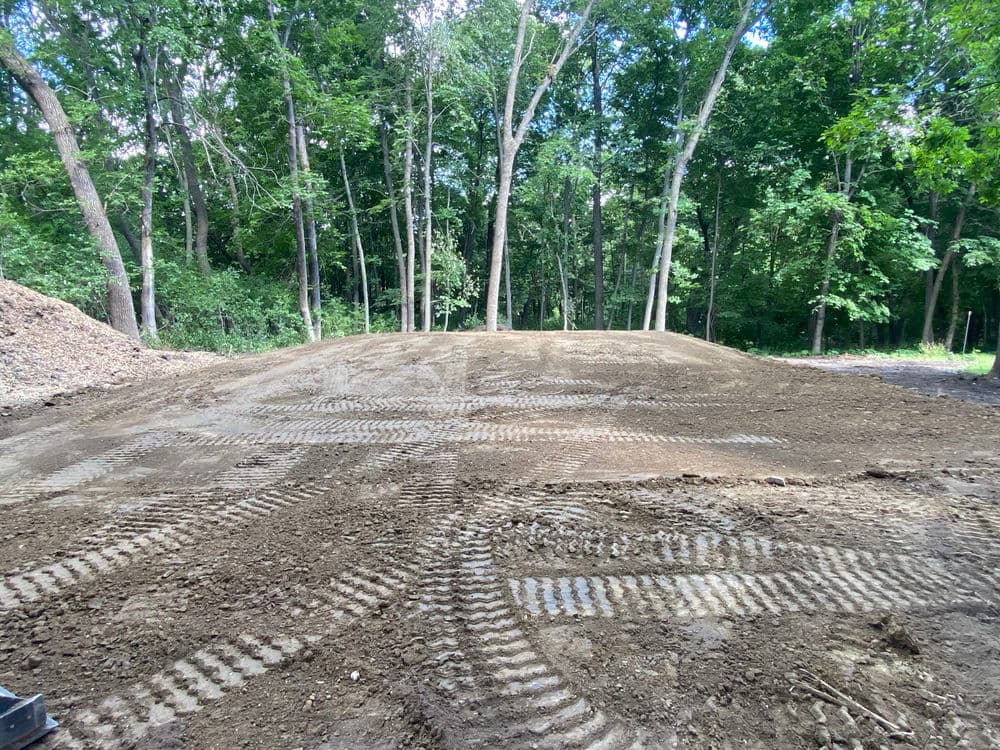 Cleared land with tire tracks in a forested area, ready for construction or landscaping.