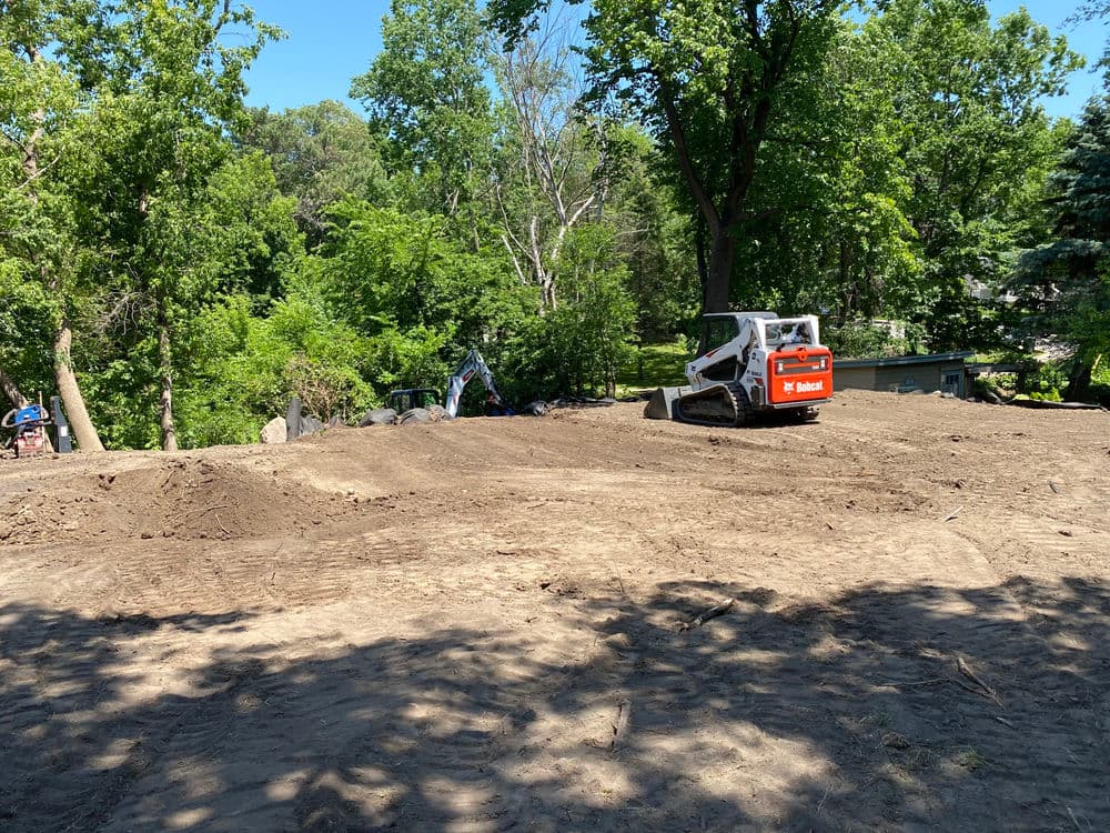 Bobcat skid steer on cleared land surrounded by trees, preparing for landscaping or construction.