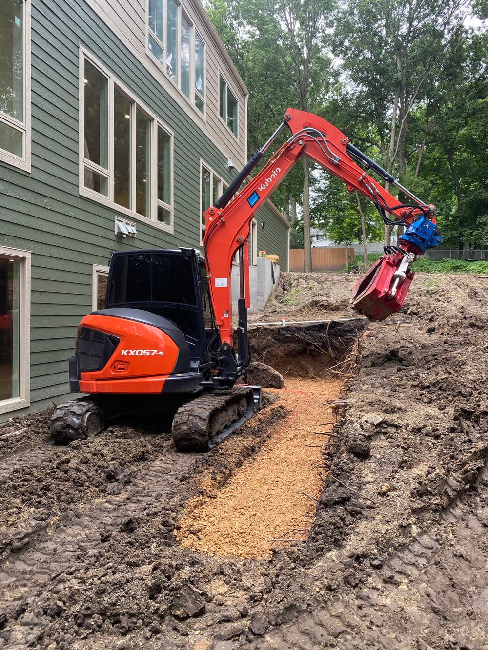 Excavator digging a trench in a backyard for construction or landscaping project.