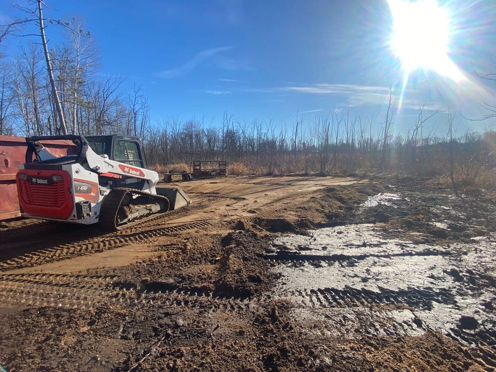 Bobcat skid steer on cleared land with tire tracks under a bright blue sky.